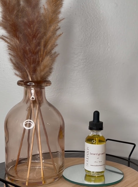 Glass diffuser with pampas grass and a bottle of Natives beard growth oil on a table.